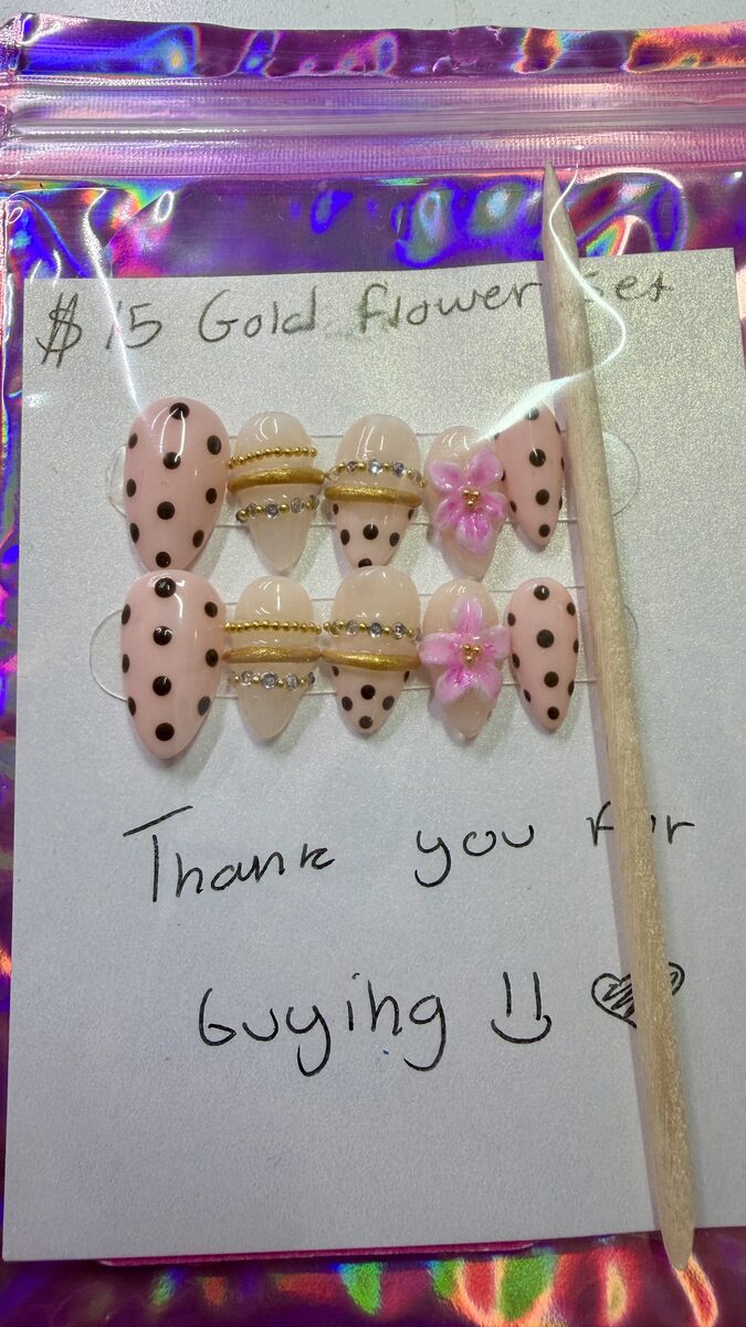 Pink and nude press-on nails with gold bands, rhinestones, black polka dots, and pink flowers